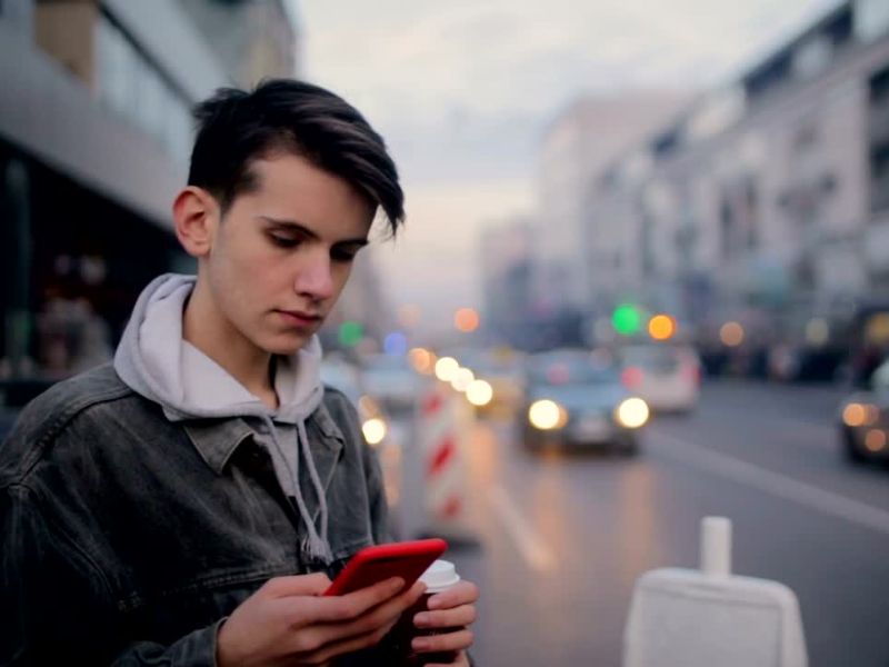 punoletni dečak na ulici koristi telefon i drći kafu u ruci
